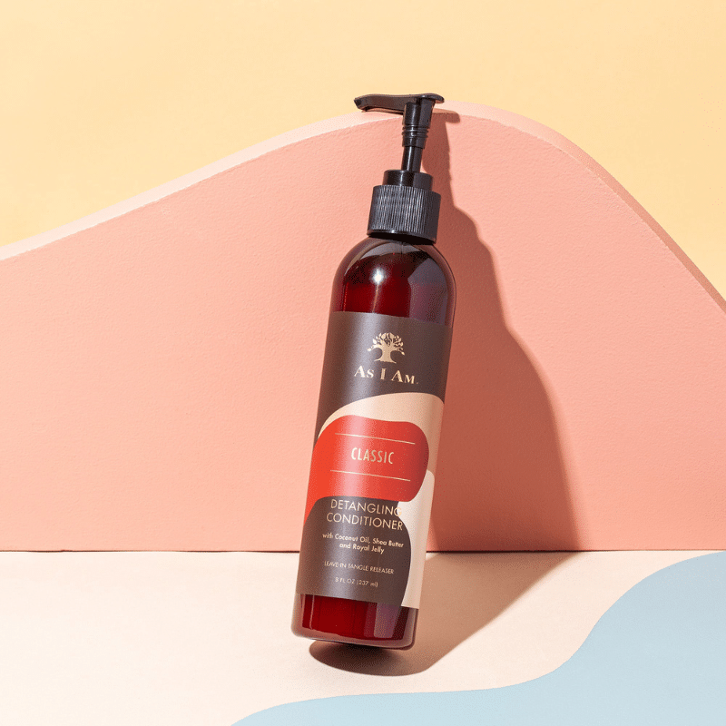 En brun flaske med en sort pumpe står på en pastelfarvet baggrund. Flasken indeholder As I Am Classic Detangling Conditioner og har en brun etiket med gul skrift.