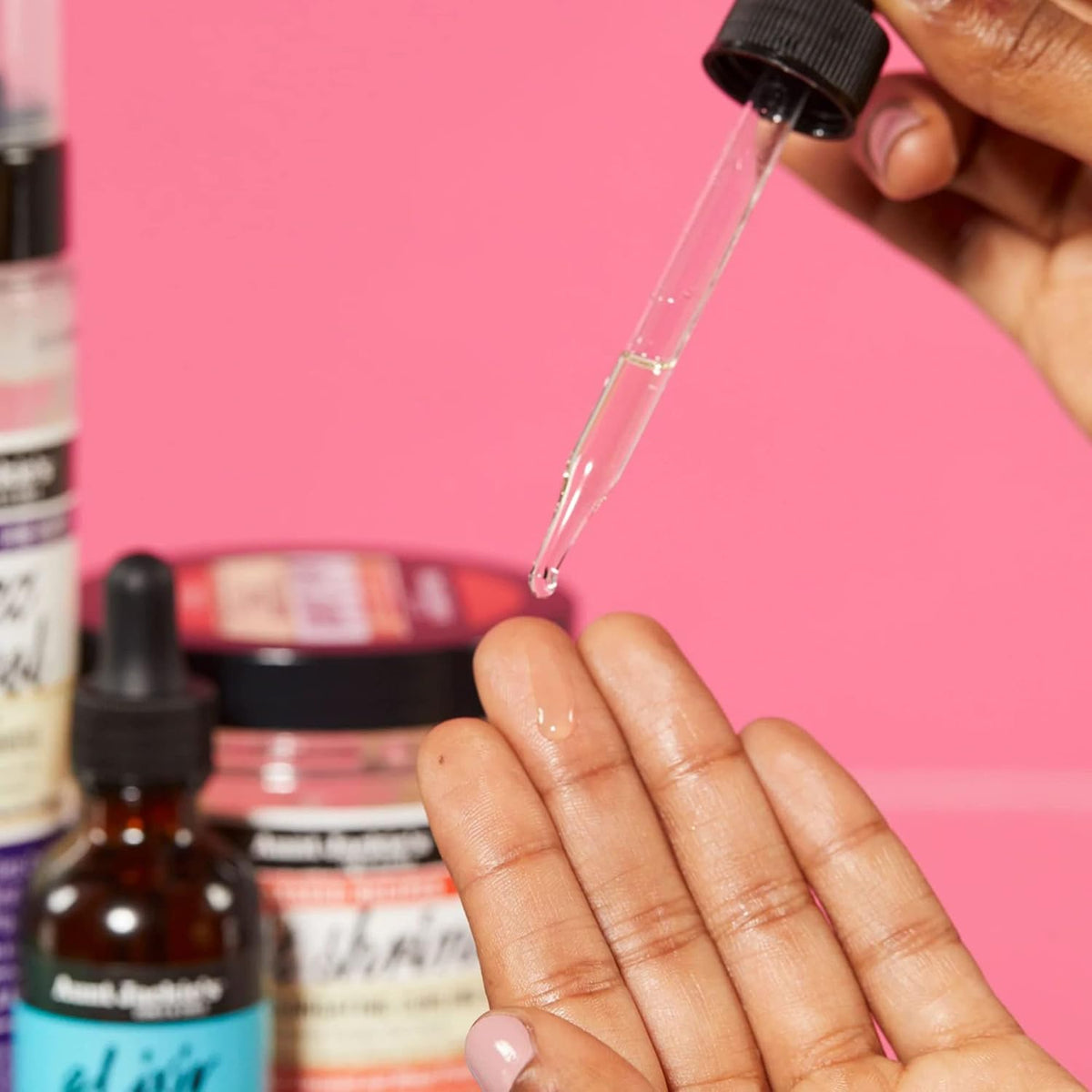 Nærbillede af en hånd, der drypper Aunt Jackie's Elixir Biotin Rosemary Hair and Scalp Oil fra en pipette på fingerspidsen.