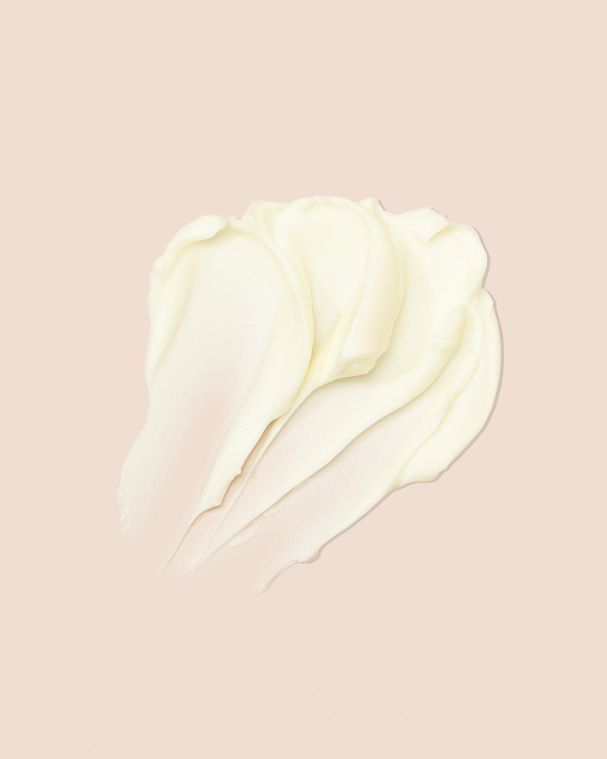 Et tæt billede af en klump hvid creme på en lyserød baggrund. Cremen er smurt ud i bløde, bølgede streger. Billedet viser indeholdet af produktet As I Am Classic DoubleButter Cream.