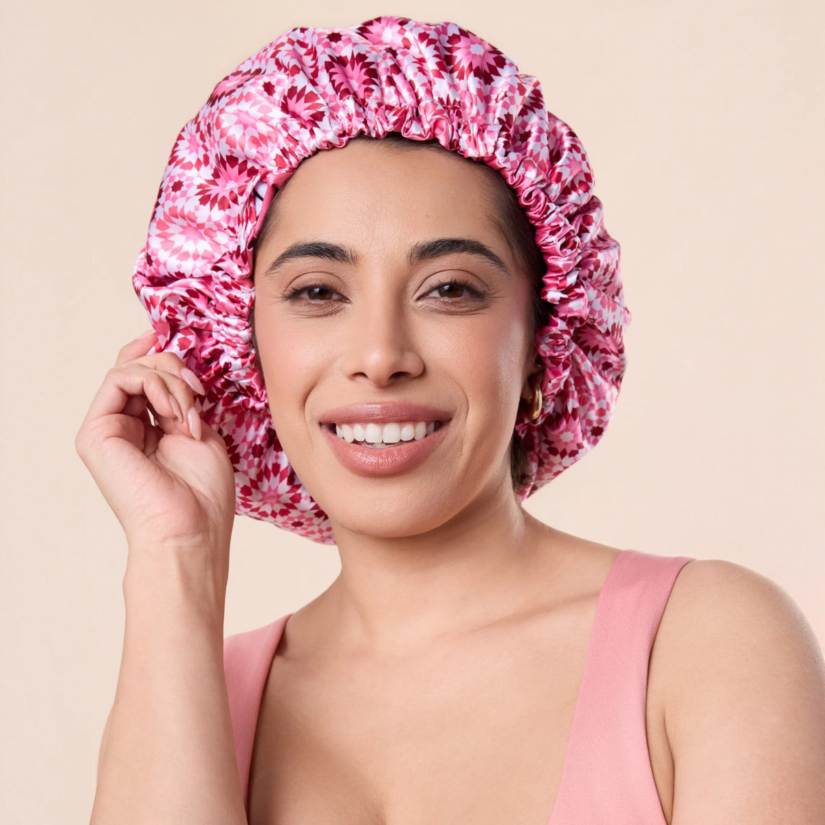 Smilende kvinde med pink mønstret satin bonnet til hårpleje, iført lyserød top.