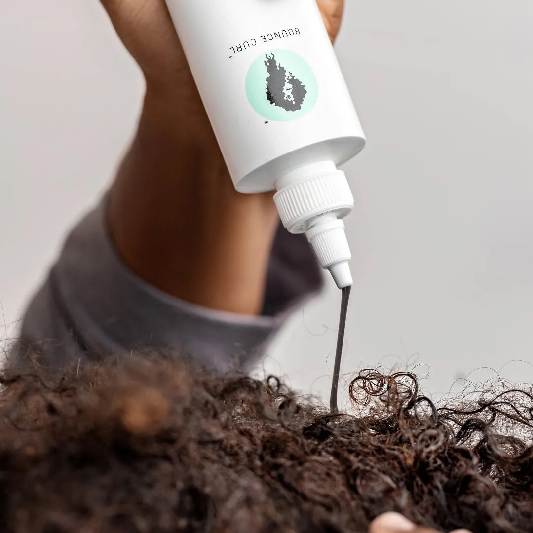 Hånd påfører Bounce Curl Tumeric Purifying Hair & Scalp Mask 237ml direkte i krøllet hårbund med præcis applikationsspids.