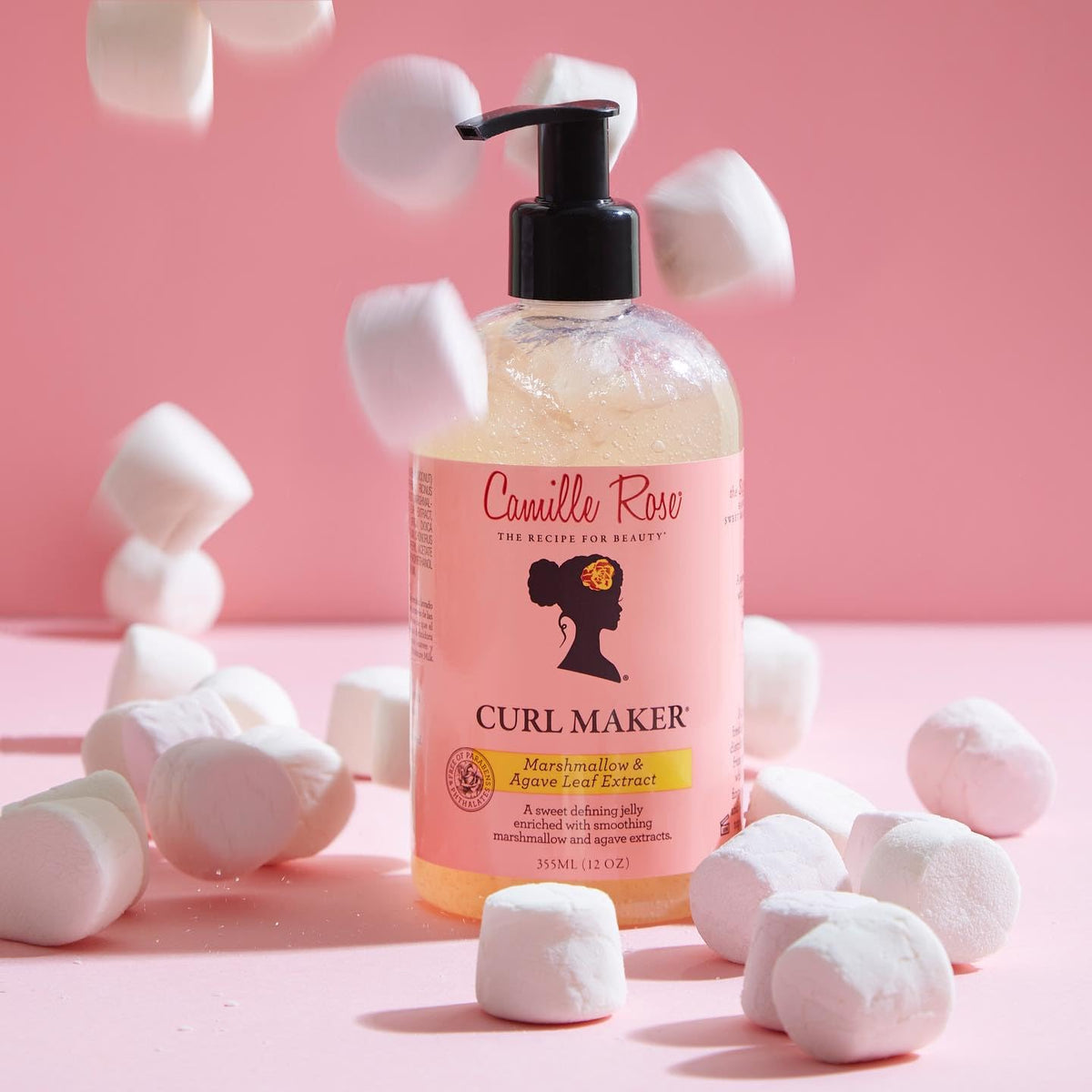 Produktfotografi af Camille Rose Curl Maker hårgelé. Flasken er placeret på en lyserød baggrund med små, hvide marshmallows, der falder ned omkring den.