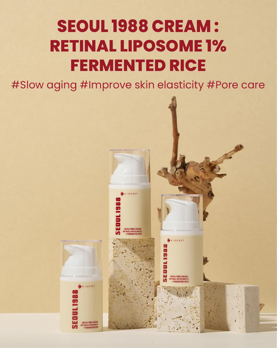 Tre flasker K-Secret Cream: Retinal Liposome 1% + Fermented Rice 50 ml står på lyse sten foran beige baggrund.